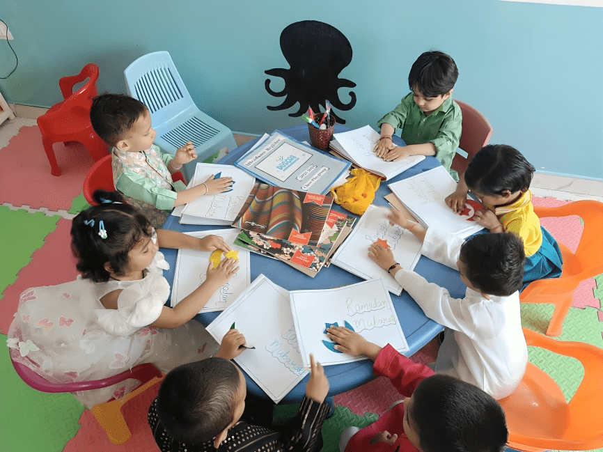 Children sitting around a table in a classroom, engaging with brain development games and writing in notebooks.