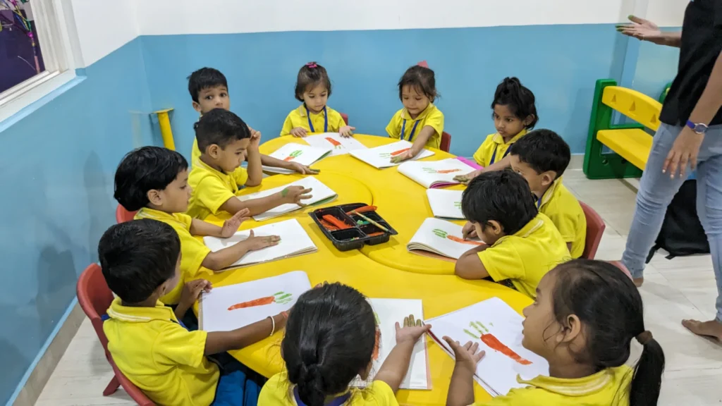 Group of young children in yellow uniforms participating in a hand-painting activity at a preschool, sitting around a round yellow table