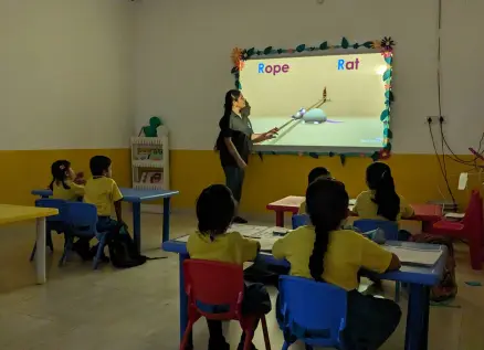 Teacher using a projector to teach phonics to young students in a classroom setting.